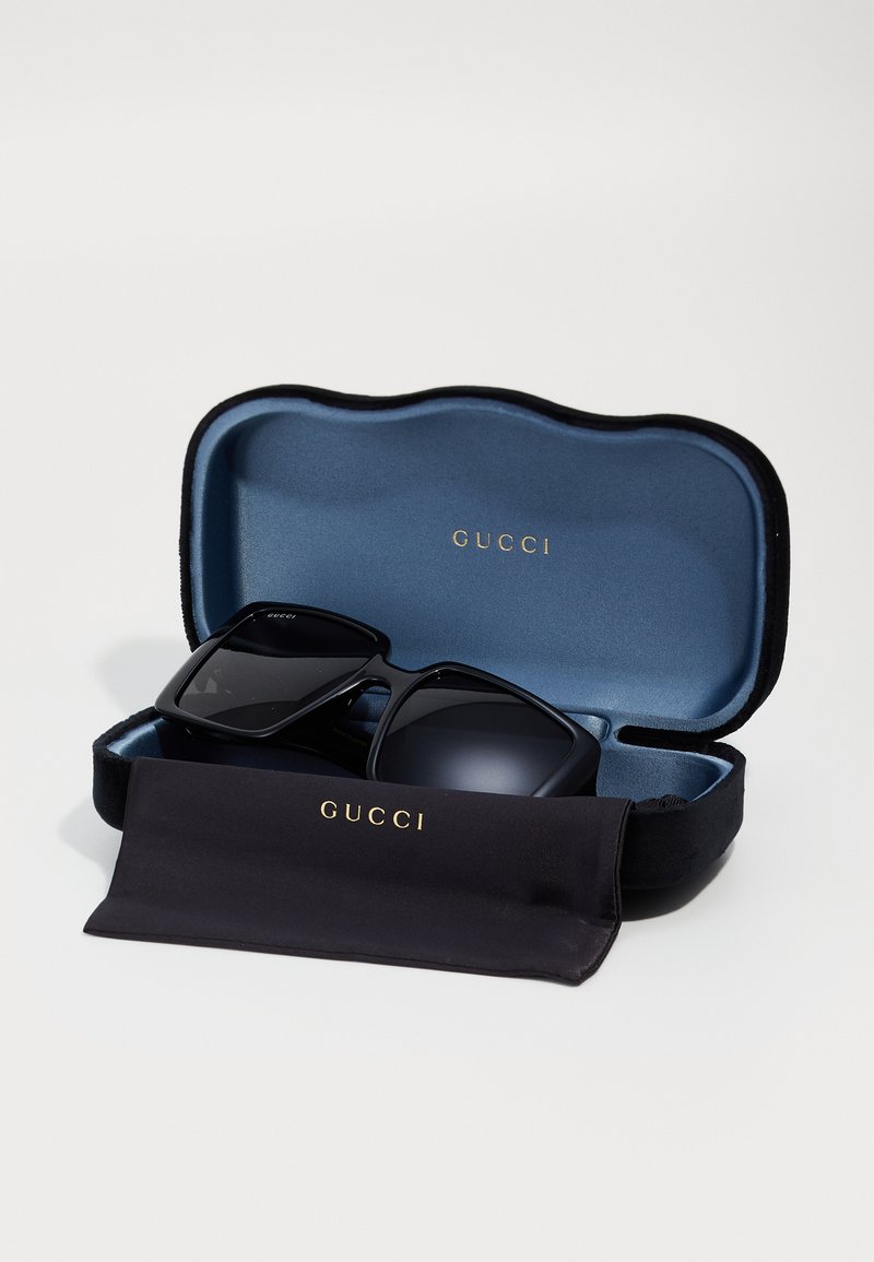 Schwarze Gucci-Sonnenbrille mit quadratischen Gläsern in offenem blau samtgefüttertem Etui und schwarzem Reinigungstuch mit goldenem Gucci-Logo.
