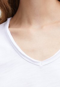White T-shirt with a V-neck design, featuring a soft texture and raw edge detailing along the neckline. Close-up of collar area.