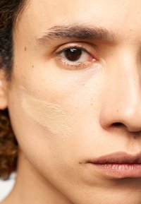 Fondotinta liquido nella tonalità beige chiaro applicato sulla pelle. Primo piano della texture della pelle, superficie liscia e tratti del viso visibili.