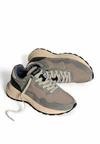 Un paio di sneakers HOFF grigie e beige con suole spesse e lacci, uno dei quali è slacciato, su sfondo bianco.