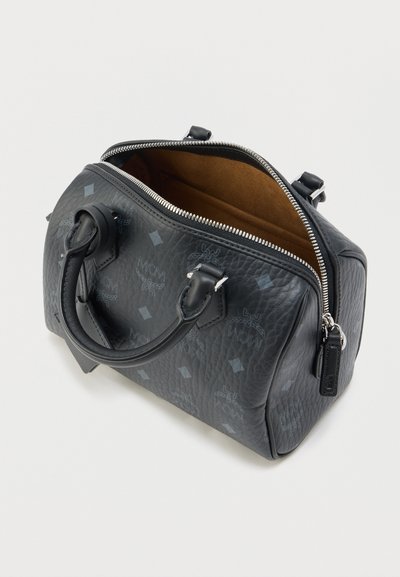 Melnas teksturētas ādas rokassomiņa ar divām rokturiem, daļēji atvērta sudraba rāvējslēdzēja, brūna zamšādas odere un atkārtotu MCM logotipu raksts.