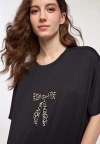 T-shirt nero con applicazione a fiocco in stampa leopardata sul petto. Il tessuto è morbido, con una vestibilità rilassata e un collo rotondo.
