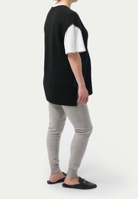 Svart stickad väst över en vit t-shirt, grå leggings och svarta slips-on skor. Outfiten har en avslappnad passform med en mjuk textur.