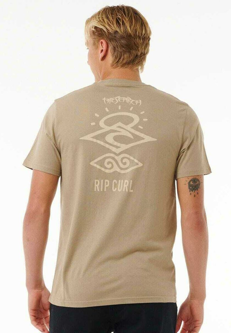 T-shirt in cotone beige con un design grafico che presenta simboli e la scritta "RIP CURL" stampata in colori chiari sul retro. Maniche corte, colletto tondo.
