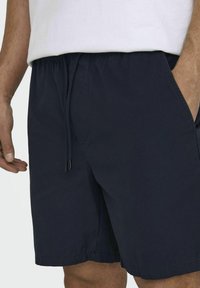 Shorts con coulisse di colore blu navy, realizzati in tessuto leggero, dotati di tasche laterali e una vestibilità comoda, con una superficie liscia e bordi orlati.