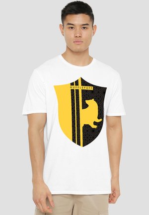 Young man wearing white t-shirt with large yellow and black Hufflepuff crest featuring a badger silhouette on the front.