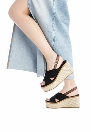 Sandalias de cuña de ante negro con una plataforma de yute trenzado, que cuentan con correas de tobillo ajustables en marrón y un diseño de punta abierta.