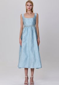 Robe midi bleu clair avec une surface texturée, décolleté carré et bretelles larges. Présente une ceinture décorative à la taille et s'évase délicatement au niveau de l'ourlet.