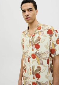 Cămașă cu mâneci scurte dintr-un material ușor, având un fundal crem și un model floral colorat în tonuri de roșu, verde și bej.