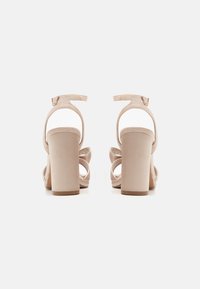 Nude sandaler med klack, flera remmar och en anklarrem. Slät tygöverdel med en texturerad innersula för komfort.