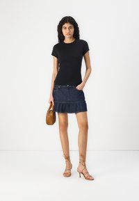 Zwarte t-shirt met korte mouwen, denim mini-jurk met rand, tan gevlochten handtas en beige sandalen met hakken en bandjes.
