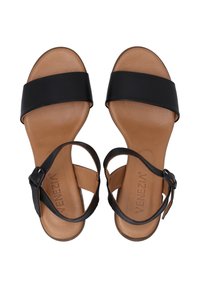 Zwarte leren sandalen met brede banden en enkelgesp, met een tan voetbed en een strak minimalistischer ontwerp. Platte zool met lichte textuur.