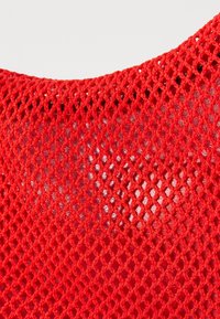 Un tissu en maille rouge présente un motif en losange avec une surface texturée, offrant transparence et légèreté.