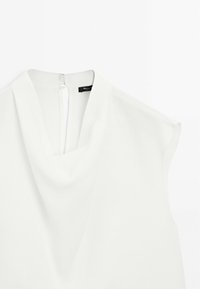 Chemisier blanc sans manches à encolure drapée et fermeture boutonnée au dos, présenté sur un fond blanc uni.