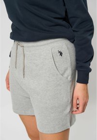 Šedé bavlněné šortky s elastickým pasem, šňůrkou a postranními kapsami. Na levé kapse je malé černé logo.