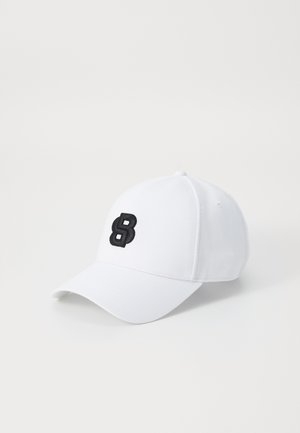 Witte baseballpet van katoen met een gebogen klep. Heeft aan de voorkant een verhoogde zwarte geborduurde letter "B".