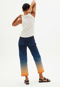 White sleeveless top, navy blue pants with an orange gradient hem, and black sandals. Smooth fabric and structured fit with back pockets.