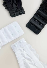 Dva čierne predlžovače na podprsenku a dva biele predlžovače na podprsenku zobrazujúce háčiky a prišité krajkové okraje na neutrálnom pozadí.