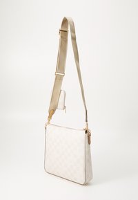 Beige rutete crossover veske med en glatt tekstur, gullfarget hardware og justerbar rem. Inkluderer en liten matchende glidelåspose.