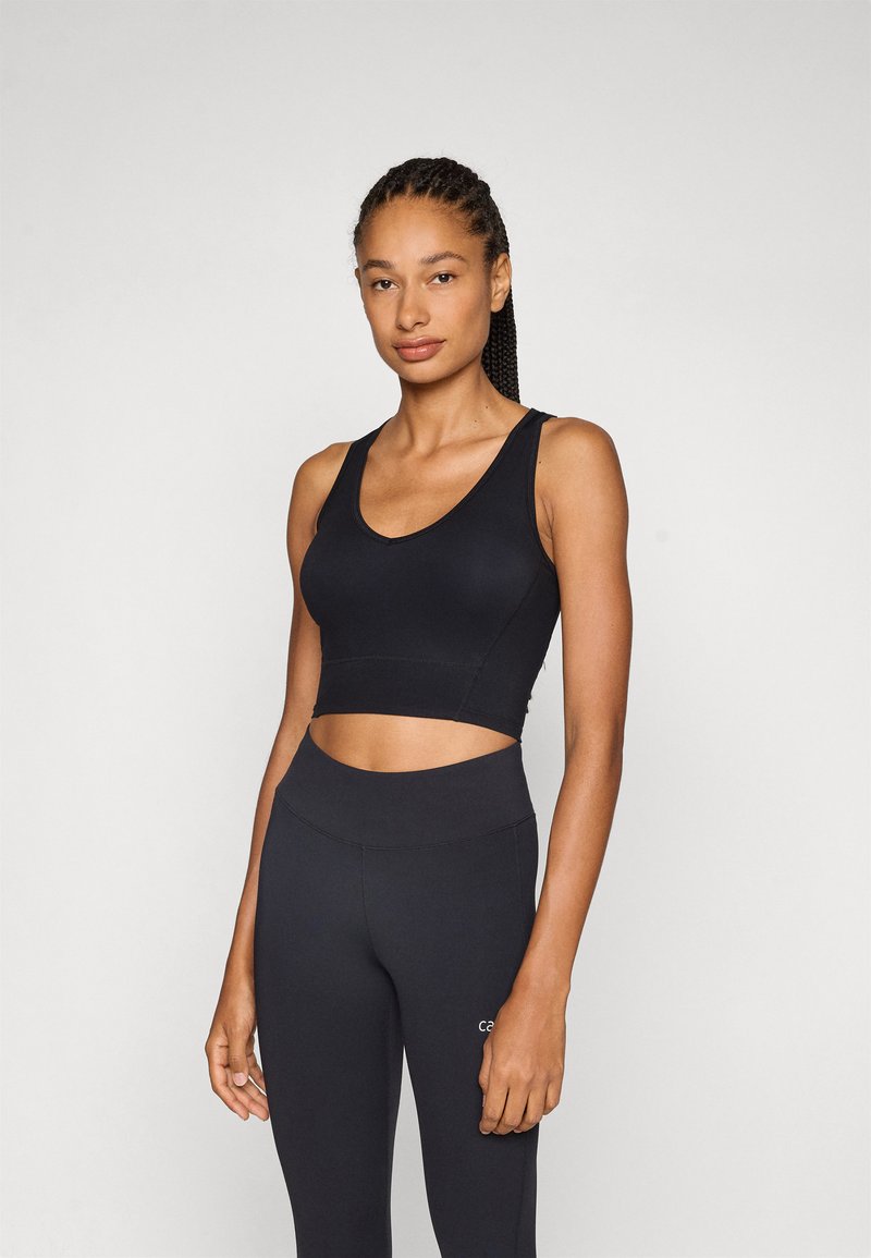 Soutien-gorge de sport noir avec un design en V, silhouette ajustée et bretelles larges. Associé à un legging noir à taille haute, texture sans couture.