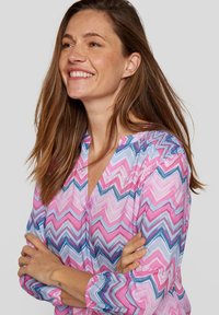 Bluse mit rosa und blauen Zickzack-Muster, V-Ausschnitt und gerafften Ärmeln. Leichter Stoff mit glatter Textur.