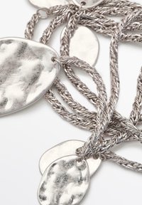 Silver jewelry necklace with braided chain links, featuring unevenly shaped, polished metal pendants with a textured surface.