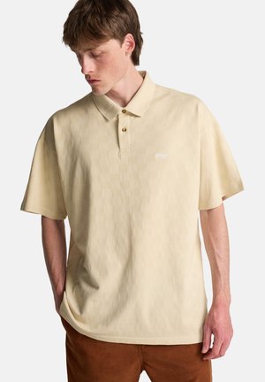 Hellgelbes Poloshirt mit kurzen Ärmeln, versehen mit einem strukturierten karierten Muster und zwei Messingknöpfen am Kragen. Kleines Logo auf der Brust.