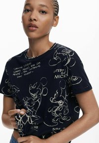 Marineblauwe T-shirt met witte schetsen van Mickey Mouse en tekst. Korte mouwen, ronde halslijn, zacht materiaal met een comfortabele pasvorm.