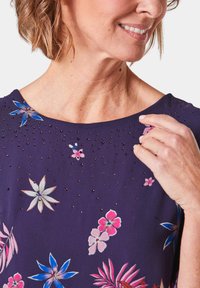 Paarse bloemen top met ingelegde rhinestones, met grote bloemen in blauw en roze tinten, ronde halslijn en een gladde textuur.