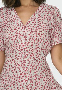 Floral dress with a V-neck, short sleeves, and button closure. Light pink fabric with small red flowers and green leaves throughout.