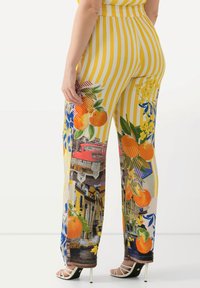 Pantaloni a gamba larga a righe gialle e bianche con motivi floreali e di frutta, caratterizzati da vivaci arance e fiori blu. Tessuto leggero, stampa dettagliata.