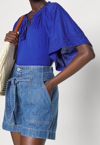 Blusa blu ricamata con maniche corte e voluminose abbinata a pantaloni shorts in denim a vita alta con vita legata e tasche laterali.