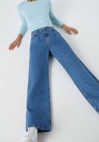 Suéter de color azul claro y textura, combinado con jeans anchos y desgastados de color azul. Los jeans tienen una cintura alta y están estilizados con zapatos blancos.