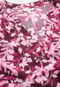 V-hals blouse in een donker burgundy stof versierd met roze bloemenpatronen en bladvormen, met een gladde textuur en subtiele glans.