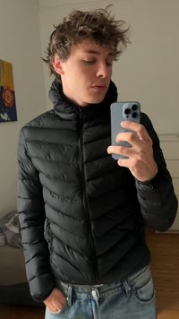 Casaco puffer preto com gola alta, textura acolchoada horizontal e fecho de correr à frente. Combinado com jeans de lavagem clara.