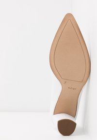 Semelle d'une chaussure à talon haut pointue beige de taille 5 avec la marque "högI", présentée sur un fond blanc.