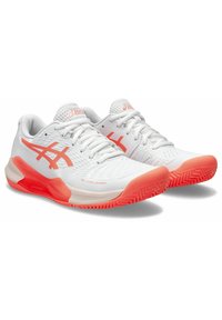 Zapatillas deportivas blancas con acentos en rosa, parte superior texturizada y detalles perforados. Cuenta con una suela de goma con un patrón de banda distintivo.