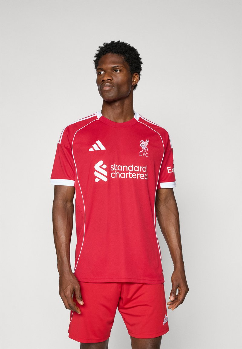 Tricou de fotbal roșu cu accente albe, având logo-ul Liverpool FC și logo-ul sponsorului "Standard Chartered". Mâneci scurte, material ușor.