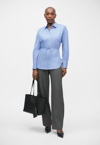 Μπλε και λευκή ριγέ πουκάμισο με κουμπιά, γκρι καρό παντελόνι, μαύρη τσάντα tote και κομμωμένα μαύρα τακούνια. Λείο ύφασμα και ψηλόμεση εφαρμογή.