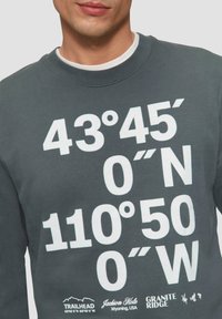 Ciemnoszara bluza z dużym białym napisem przedstawiającym współrzędne. Na dole znajdują się logo "Trailhead" i "Granite Ridge".