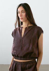 Dark purple linen top with short sleeves, a V-neckline, and an elastic hem, featuring a smooth texture and minimalist design.
