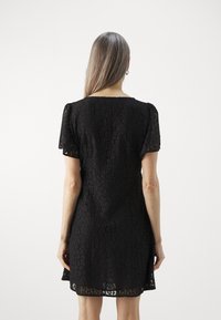 Vestido negro de encaje con mangas cortas, patrón floral y una silueta recta. Tejido ligero con un acabado texturizado y diseño hasta la rodilla.