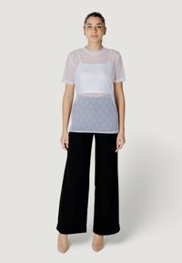 Top blanco de malla con mangas cortas, diseño en capas, acentos bordados, combinado con pantalones negros holgados y zapatos beige claros.