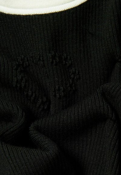 Suéter negro de canalé con un detalle de cuello blanco, que muestra un patrón texturizado y una tela suave. El material parece ser de punto y flexible.