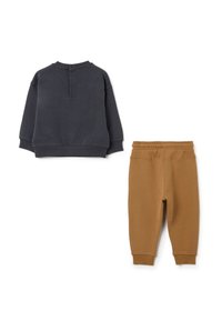 Sudadera gris oscuro con cuello redondo y detalle de botones en la parte trasera, combinada con pantalones jogger de cintura elástica en tono marrón. Ambos hechos de una tela suave y lisa.