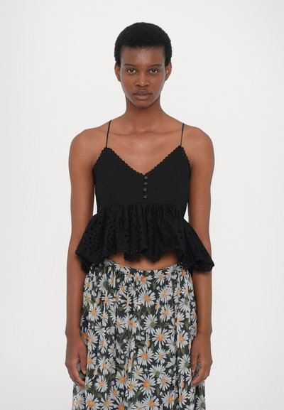 Top court sans manches noir avec un ourlet volanté, des détails de boutons et un tissu texturé. Associé à une jupe longueur genou à motif floral avec des marguerites.