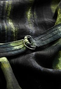 Svart tyg med gröna och blå mönster; har en silvermetallspänne och texturerad söm längs remmen.