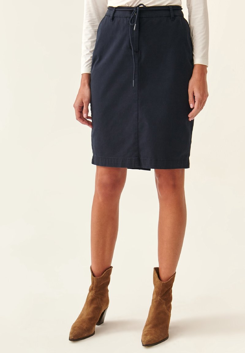Jupe bleu marine longueur genoux en coton avec taille à cordon, dotée de poches latérales et d'une coupe droite, associée à des bottines en daim marron.