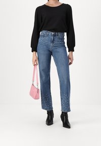 Haut noir à manches longues, jean bleu taille haute avec des embellissements en perles au bas, et bottines noires. Sac à main rose avec une bandoulière.