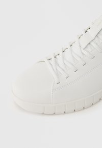 Baskets blanches avec tige en cuir lisse, bout arrondi, lacets plats et semelle en caoutchouc texturée au design segmenté.